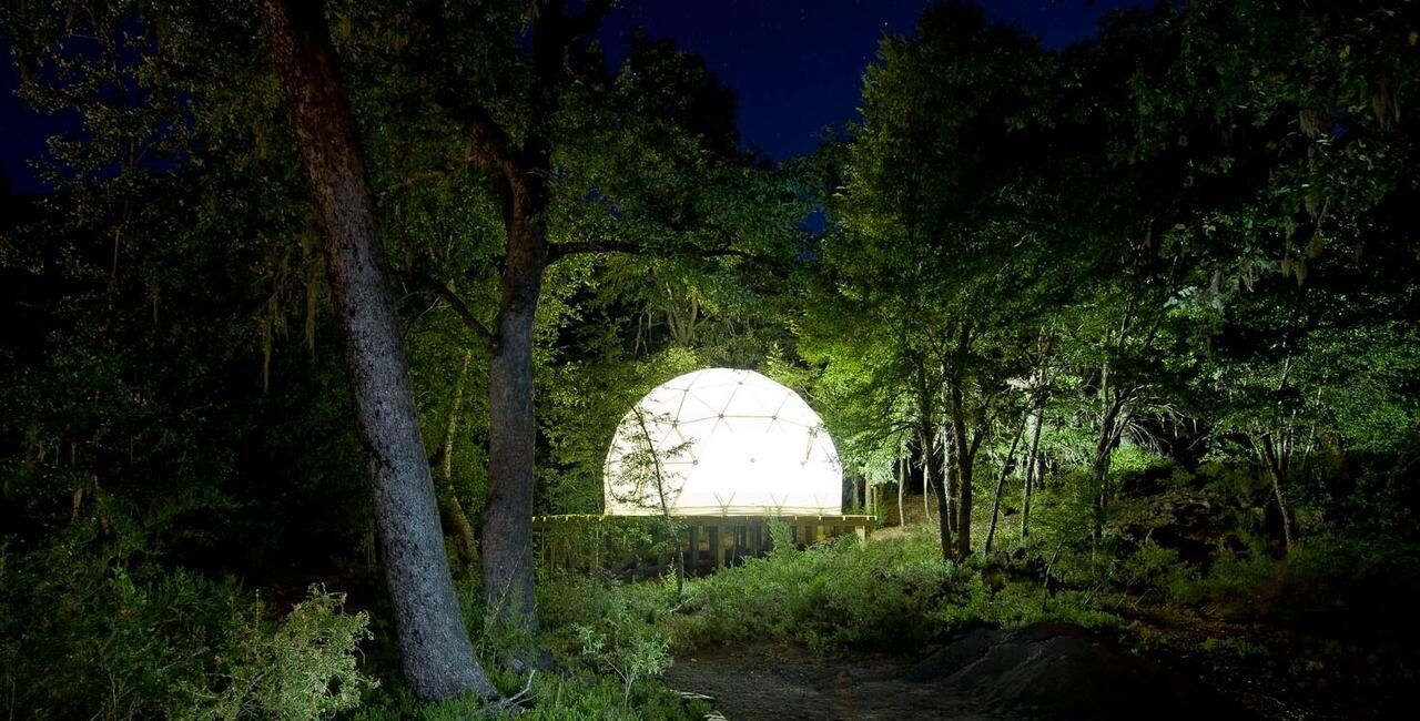 Domo iluminado por la noche en un bosque, experiencia de glamping sostenible en Chile.